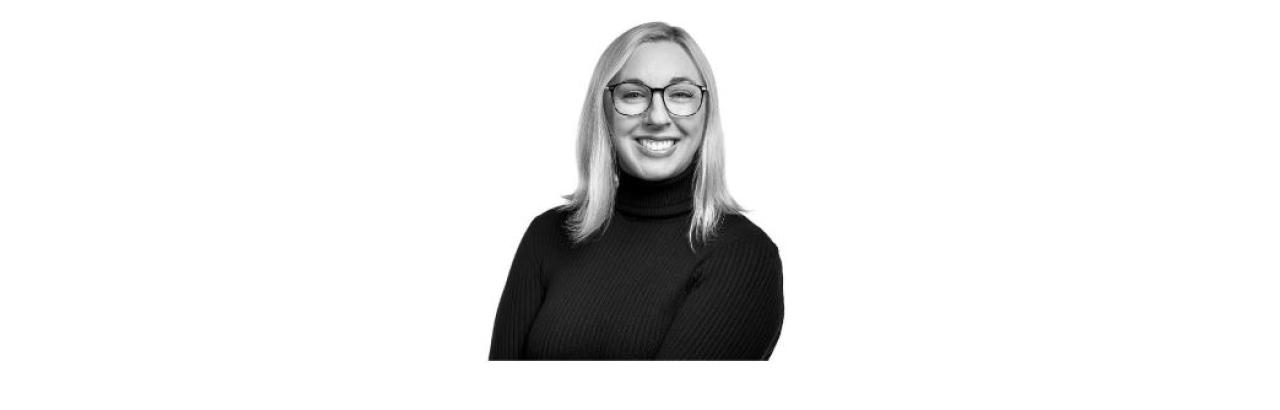 a black and white photo of Kelly Keel, a young white woman with blonde straight hair and glasses wearing a black turtleneck