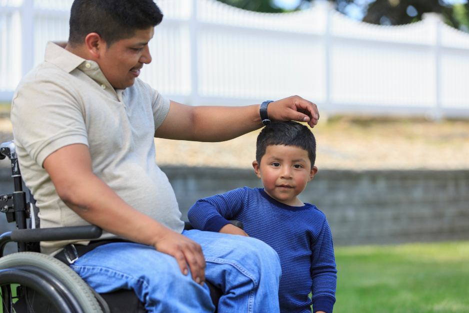A man in a wheelchair with his young son around 5 years old standing next to him. 