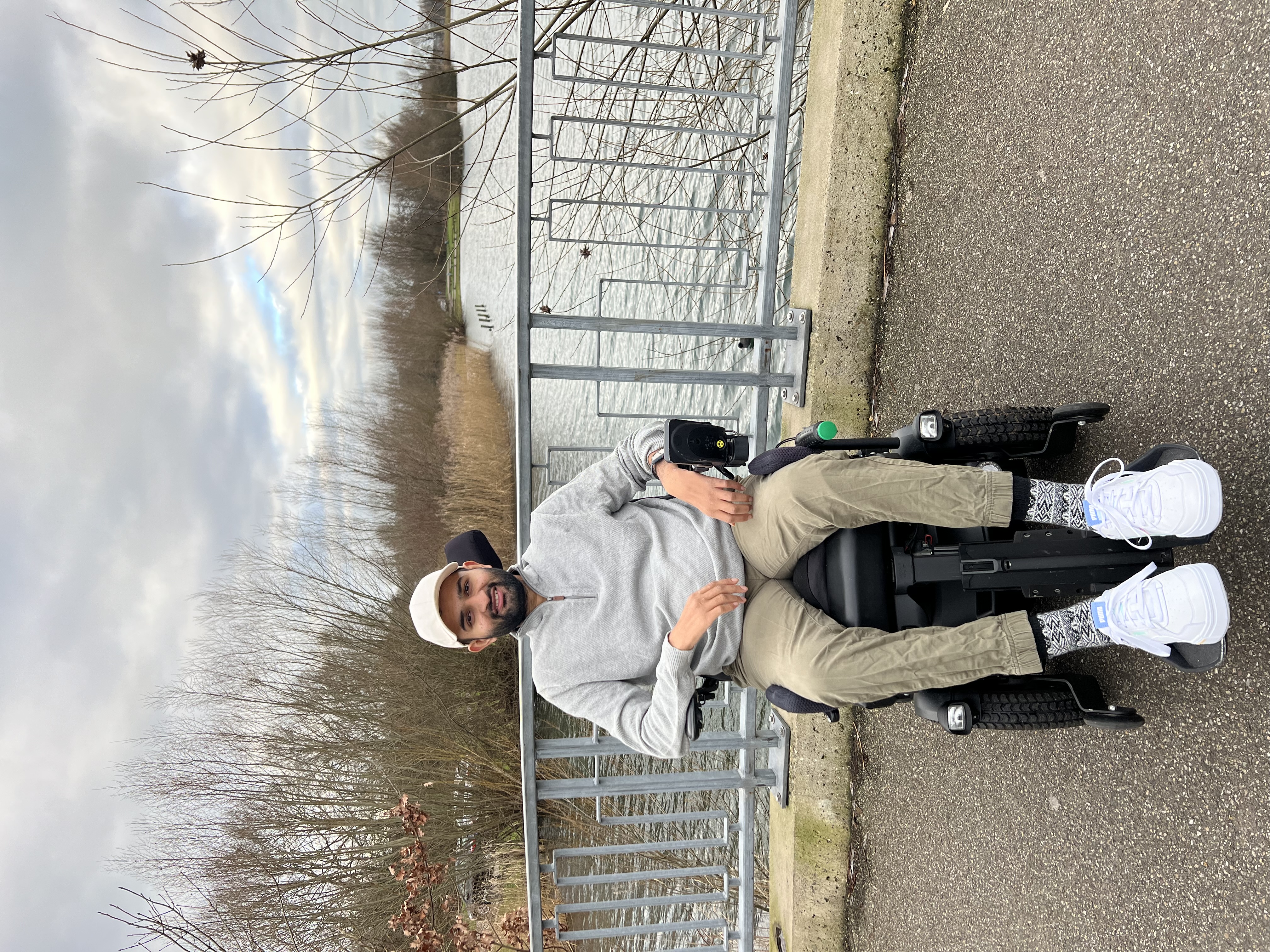 Photo of Vriaj, a young man of Indian descent, in a wheelchair on a bridge with a stream underneath.