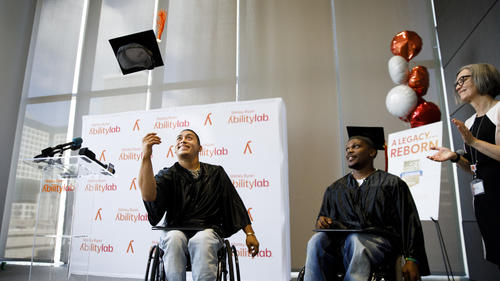 GED graduate Leomar Leyva tosses his graduation cap, while fellow graduate Charles Winters looks on.