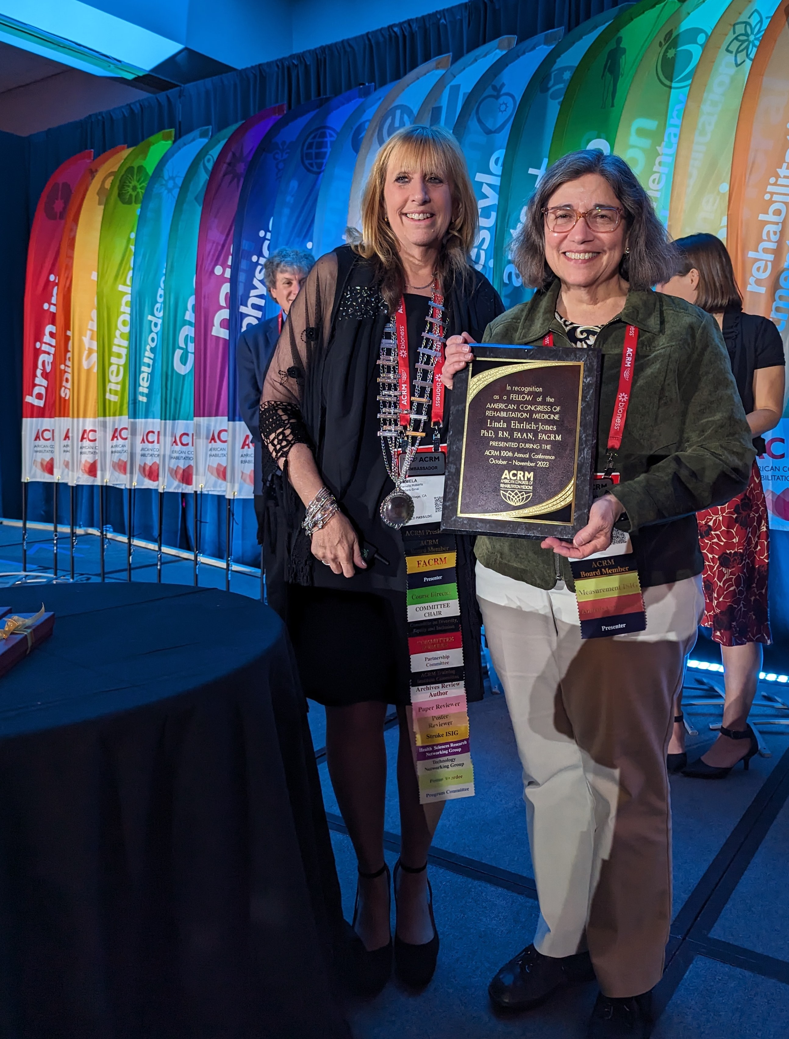 a blonde woman with a black dress stands next to a woman with short dark hair holding a plaque. They are at the ACRM Annual Conference.
