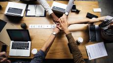 Five people join in for a handshake over a desk.