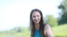 Edeth poses in front of a grass-filled landscape with a pond and trees