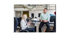 Lady in a wheelchair talking to a man sitting on a desk.