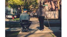 A person in a wheelchair with caregiver walking on a sidewalk