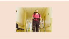 Picture of man walking in an exoskeleton in a hallway.