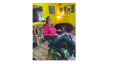 This image shows Maggie Winston in her wheelchair wearing a pink sweater and jeans. 