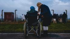 man in wheelchair talks with standing woman. Their backs are to the viewer