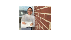 Niveda - young woman in white turtleneck smiling and leaning against a brick wall