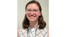 photo of a young white woman with glasses and brown shoulder-length hair smiling. She is wearing a white blouse.