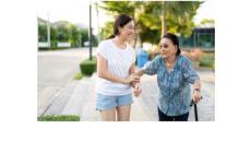a photo of a young asian woman in blue shorts and a white t shirt helping an older Asian woman in a blue blouse and black pants with a cane