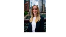 a color photo of Nicole Sharf, a young white woman with shoulder length blonde hair standing on a bridge over the Chicago River with buildings in the background
