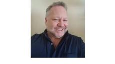 color photo of Bob Sattler, a middle aged white mad with a grey beard and grey hair wearing a black button down shirt