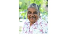 color photograph of Cindy Bently - a middle aged Black woman with short grey hair wearing a white top. She is outside and is smiling