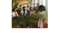 color photo of several people sitting in a circle talking. The people are Black or white and all are young.