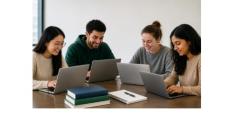 Four students looking at laptops sit together.