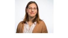 Color photo of Dalia De Santis, a young whit woman with straight brown hair and glasses wearing a tan cardigan with a red and white striped button-down short under it.