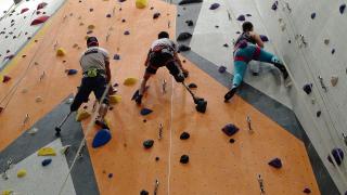 Looking up at three people climbing an indoor rock wall