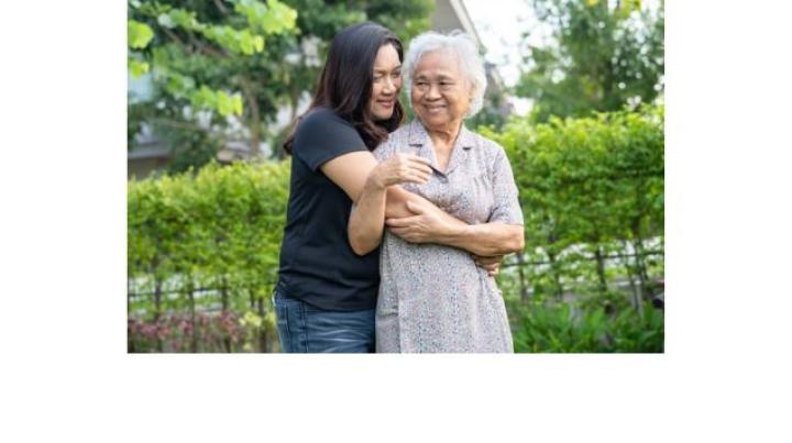 color photo of a young Asian woman in jeans and a black t shirt hugging an older Asian woman in a lavender dress