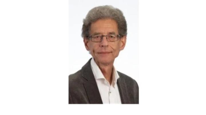 Color photo of Marcel Post, an older white man with grey curly hair and glasses wearing a black cardigan over a white shirt