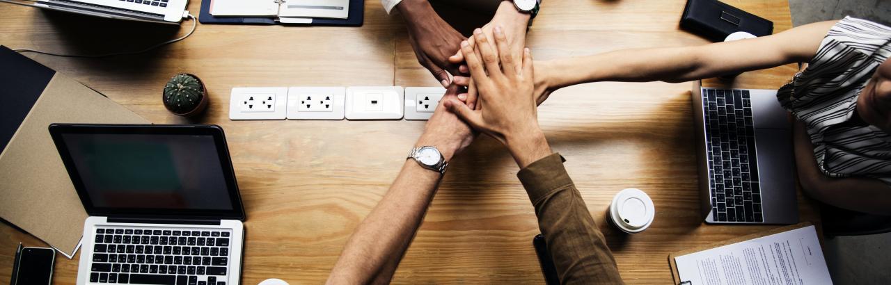 Five people join in for a handshake over a desk.