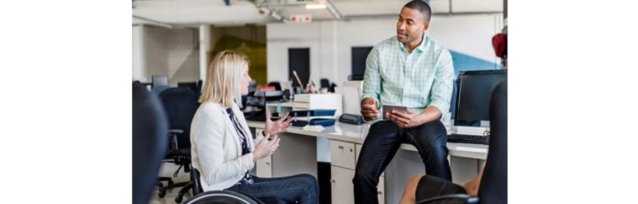 Lady in a wheelchair talking to a man sitting on a desk.