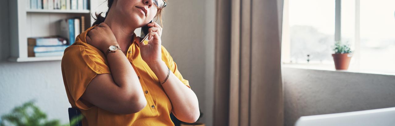 woman rubs her neck while sitting in a home office