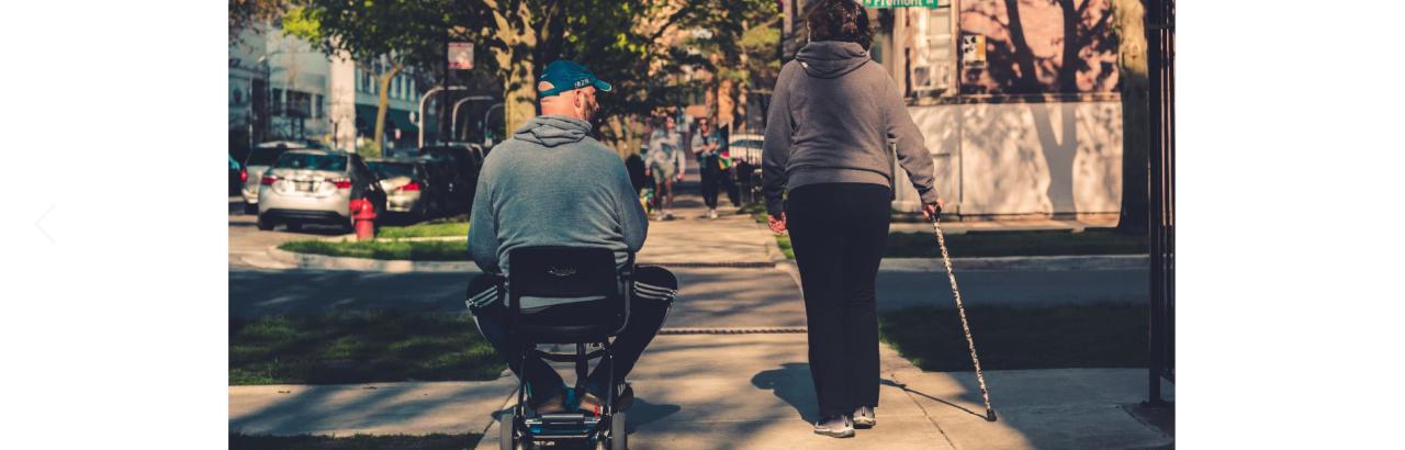 A person in a wheelchair with caregiver walking on a sidewalk