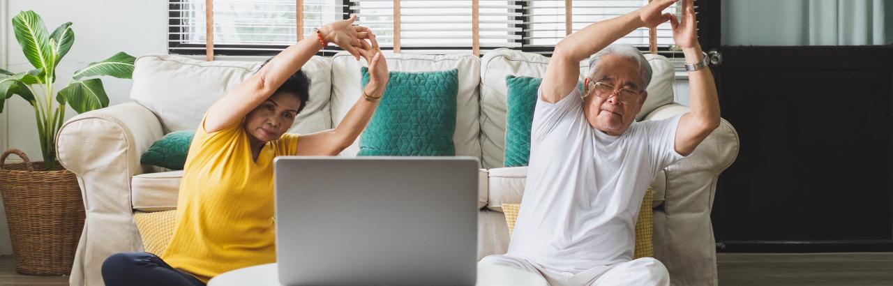 Man and woman do seated yoga at home using laptop