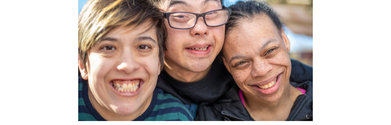 Three individuals with intellectual and/or developmental disabilities are smiling into the camera.