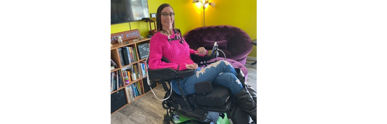This image shows Maggie Winston in her wheelchair wearing a pink sweater and jeans. 