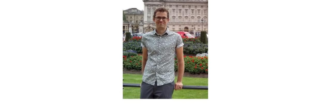 picture of man with brown hair and glasses standing in front of a building