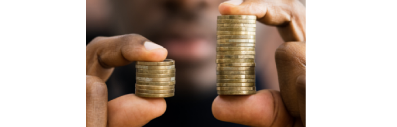 A black man is holding two stacks of gold coins in each hand. The stack of coins in the left hand is smaller than the stack of coins in the right hand. 