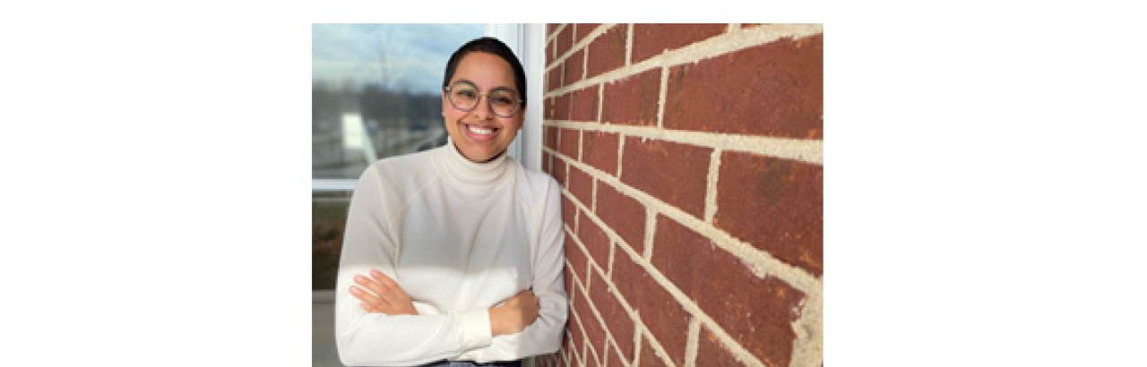 This is an image of Niveda Tennety. She is leaning against a wall and is wearing a white sweater with jeans. 