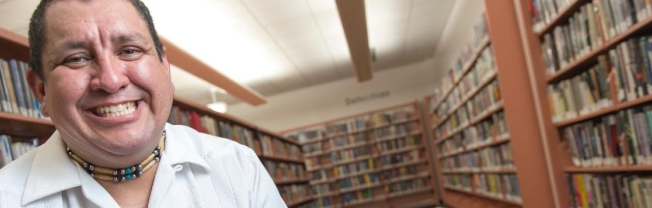 Latino man with big smile in front of shelves of books