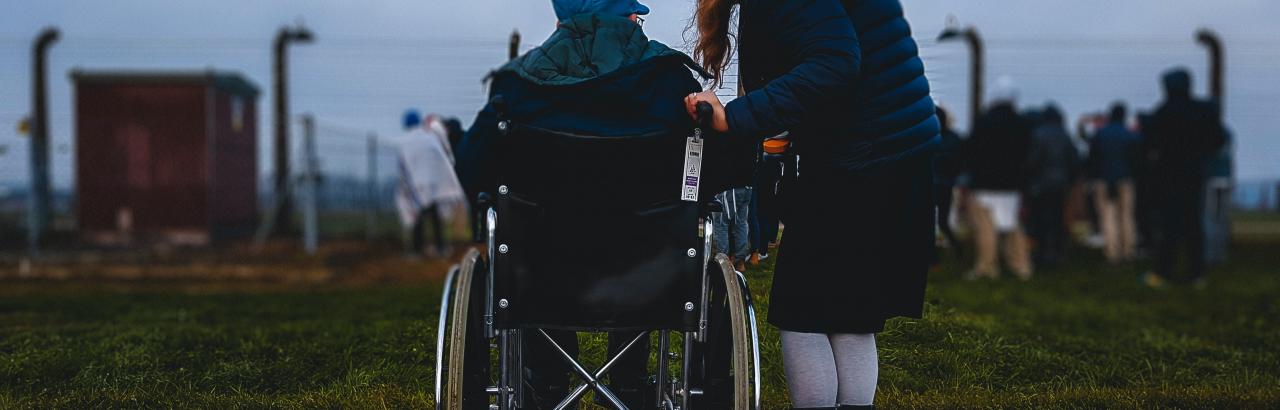 man in wheelchair talks with standing woman. Their backs are to the viewer