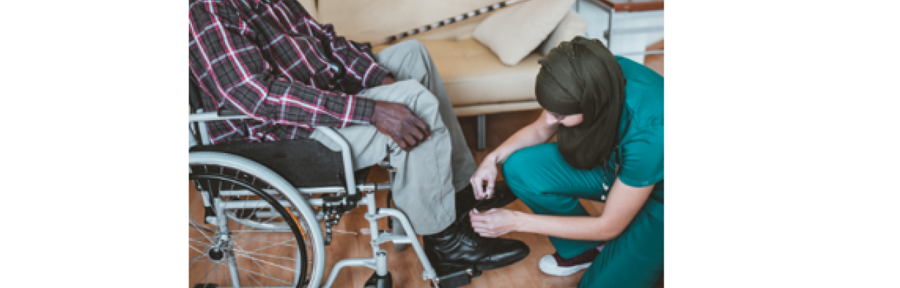 black man in wheelchair with woman in nurse clothing and headscarf adjusts his foot rest