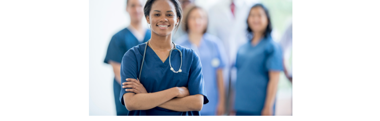 African American nurse with arms crossed and smiling with nurse colleagues in the bacground