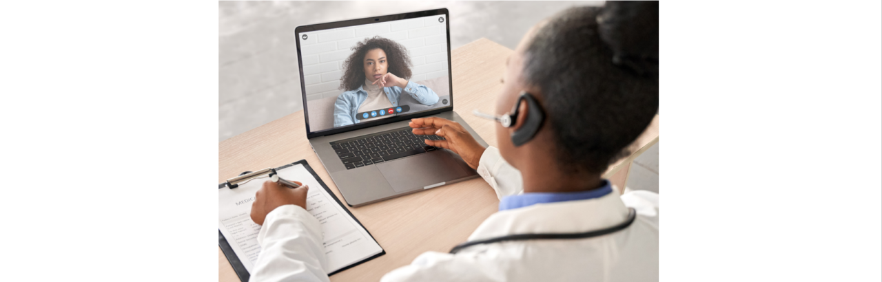 A picture of two woman who are black, one woman in wearing a white coat and one woman is on a computer screen and a carrying out a virtual conversation.