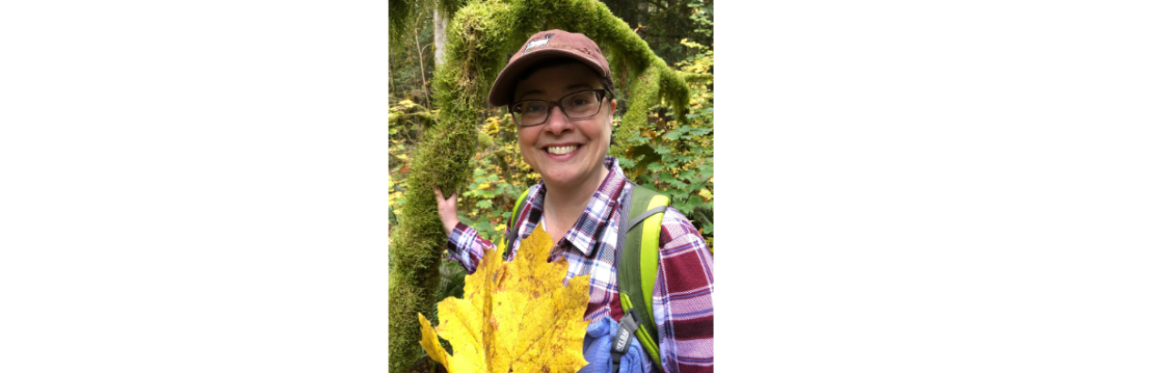 Woman with glasses smiling and holding a large leaf. She is outdoors