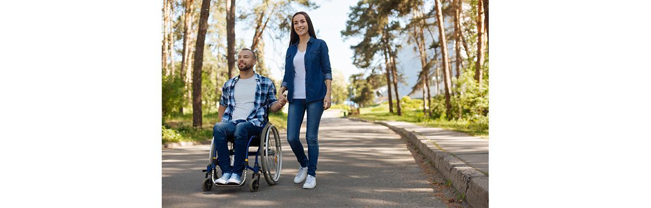 A man using a wheelchair and a woman hold hands outside.
