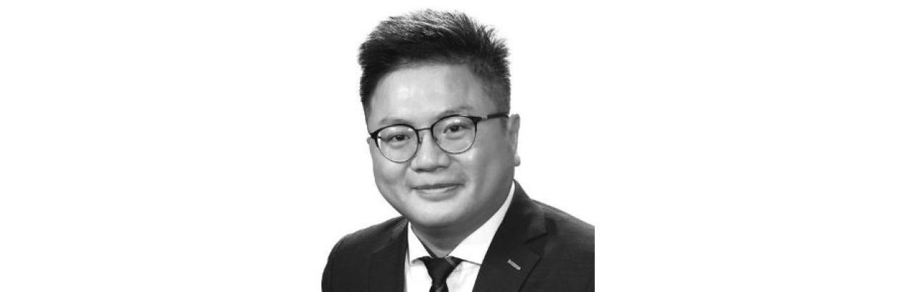 black and white photo of an Asian man with glasses and wearing a suit.
