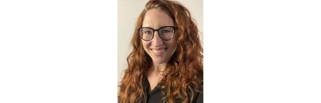 Young white woman with long red curly hair and black rimmed glasses is smiling.