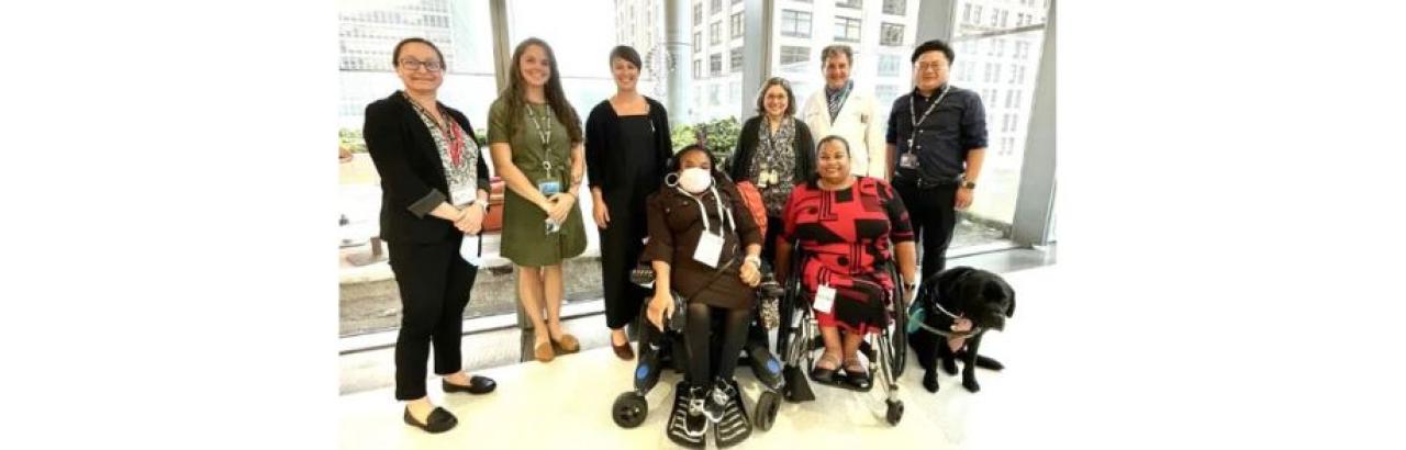 group photo of 8 people, two in wheelchairs one black service dog