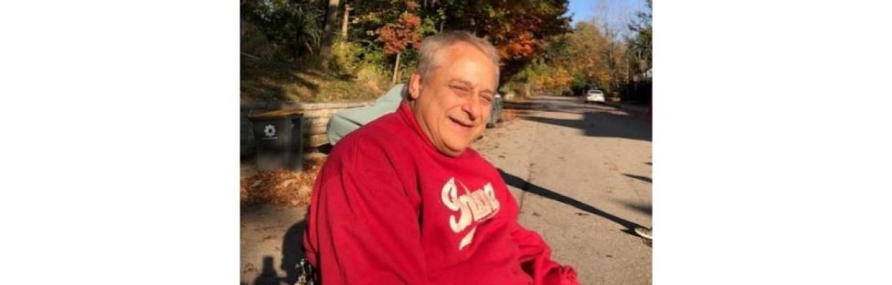 Middle aged man with grey hair wearing a read sweatshirt sitting in a wheelchair outside in Autumn