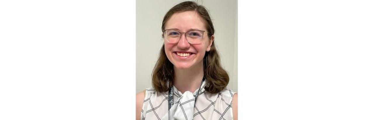 photo of a young white woman with glasses and brown shoulder-length hair smiling. She is wearing a white blouse.