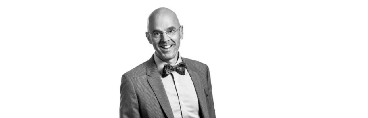 Black and white photo of white man with glasses in a suit with a bow tie