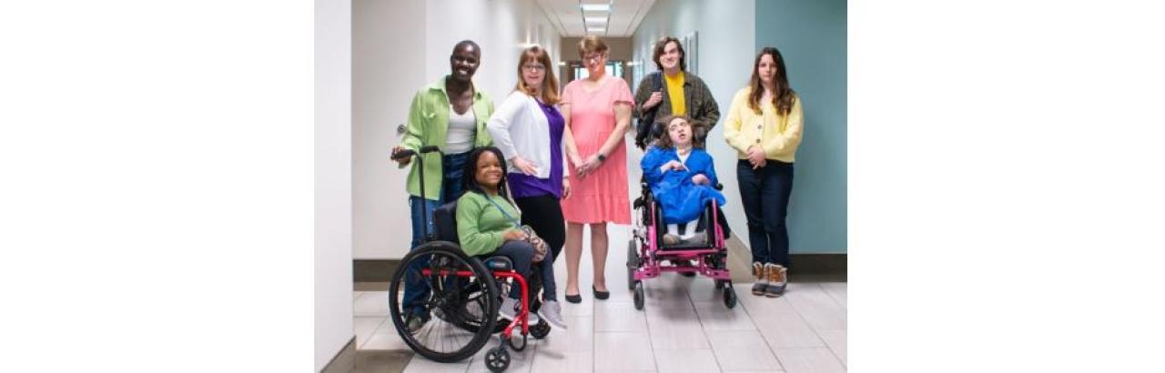 A group of people standing together in a hallway, two are in wheelchairs