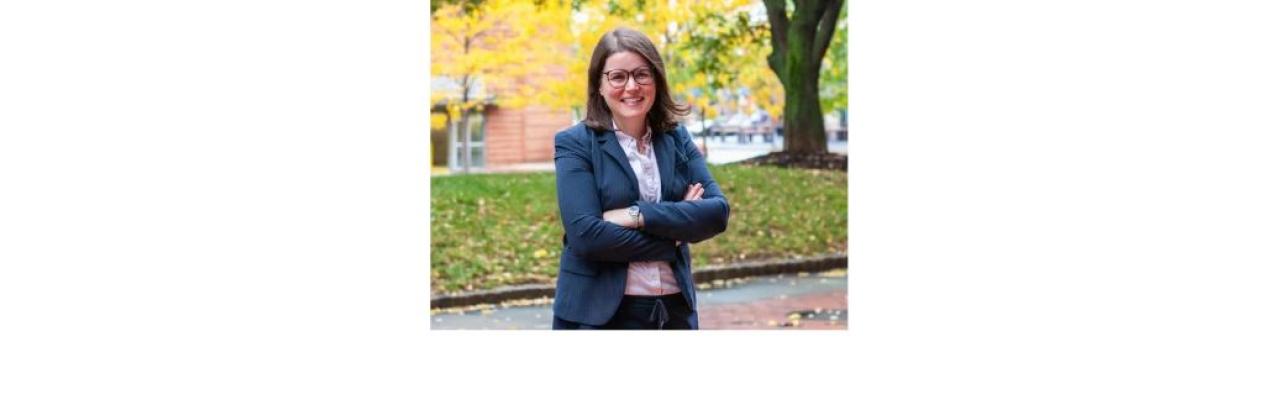 A photo of Carli Friedman, a young white woman with shoulder length brown hair and glasses standing outside