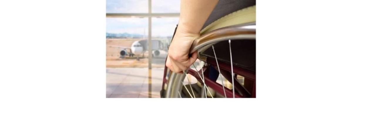 a photo of a hand holding the wheel of a wheelchair facing a window that looks out at an airplane on the tarmac